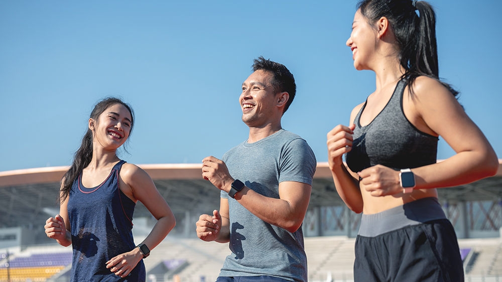 A group of cheerful Asian athlete runners enjoy a conversation while training and running at a stadium on a bright, sunny day. friendship, sport, lifestyles, leisure