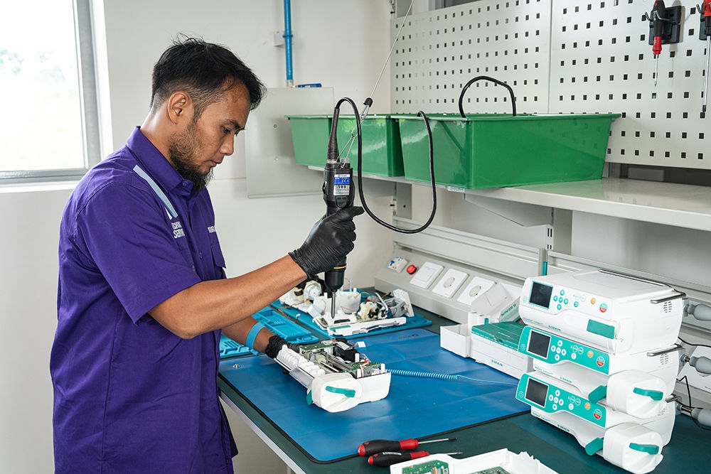 A B. Braun technical service maintenance worker is handing over a box containing replacement parts for medical devices.